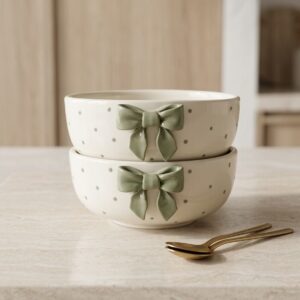 Stylish ceramic coffee mug set with green bow detailing placed on a kitchen counter with golden spoons.